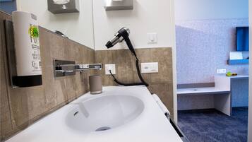 Un baño moderno con un lavamanos blanco, un secador de manos y un dispensador de toallas.