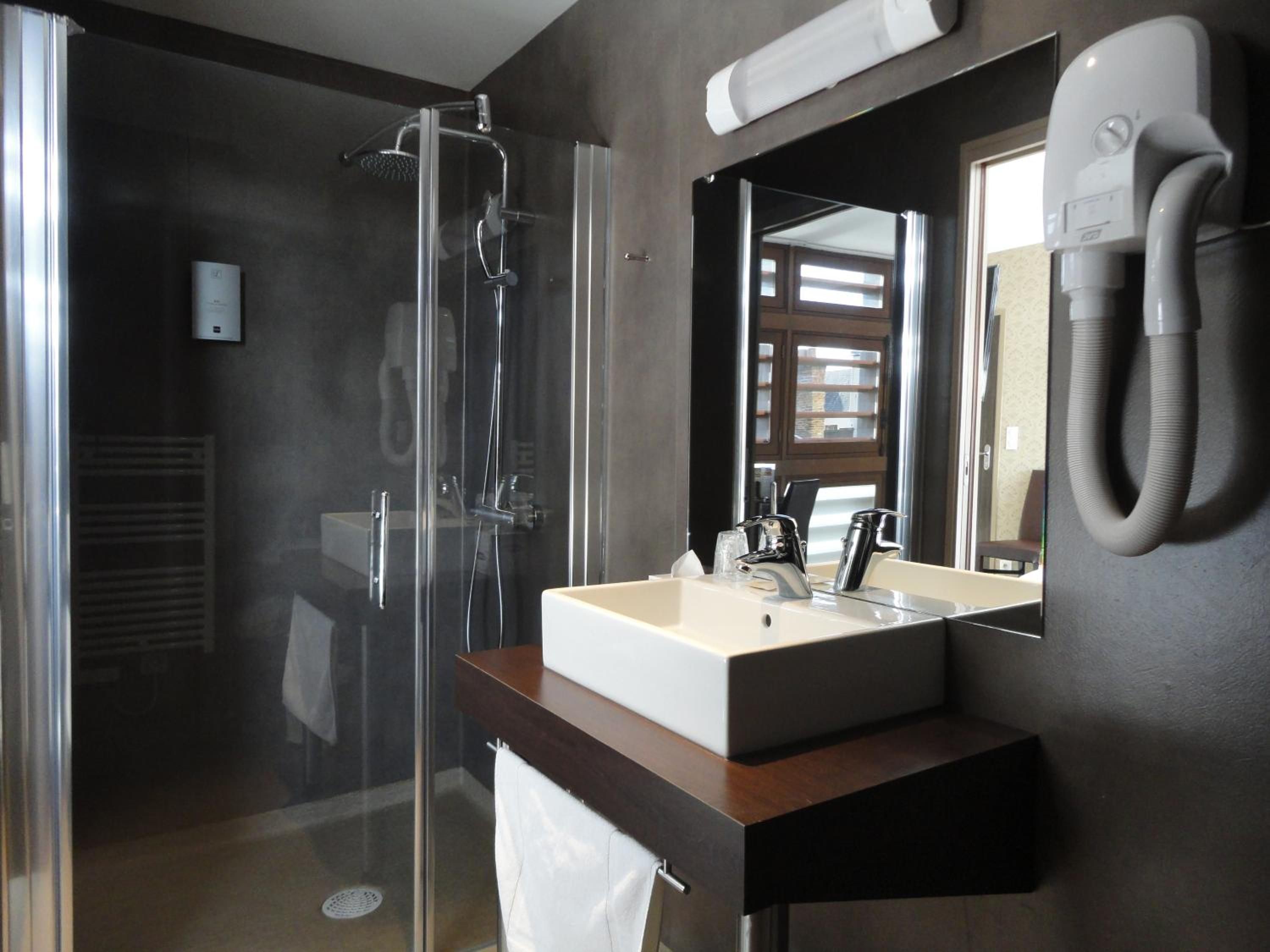 Un baño moderno con ducha envuelta en vidrio, un lavamanos con espejo y un perchero para toallas.