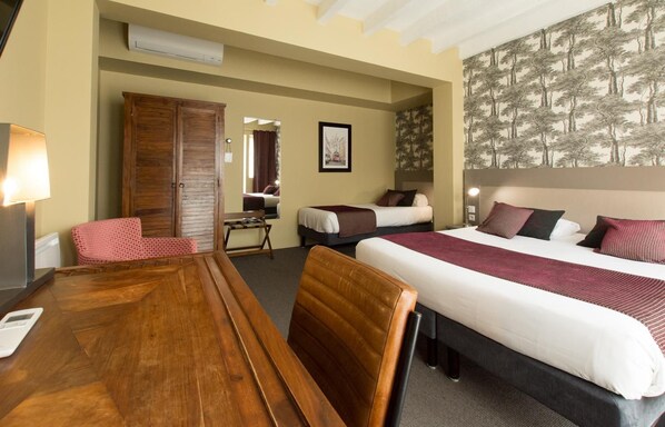 Une chambre d’hôtel avec une table à manger en bois, deux lits, une armoire et un miroir.