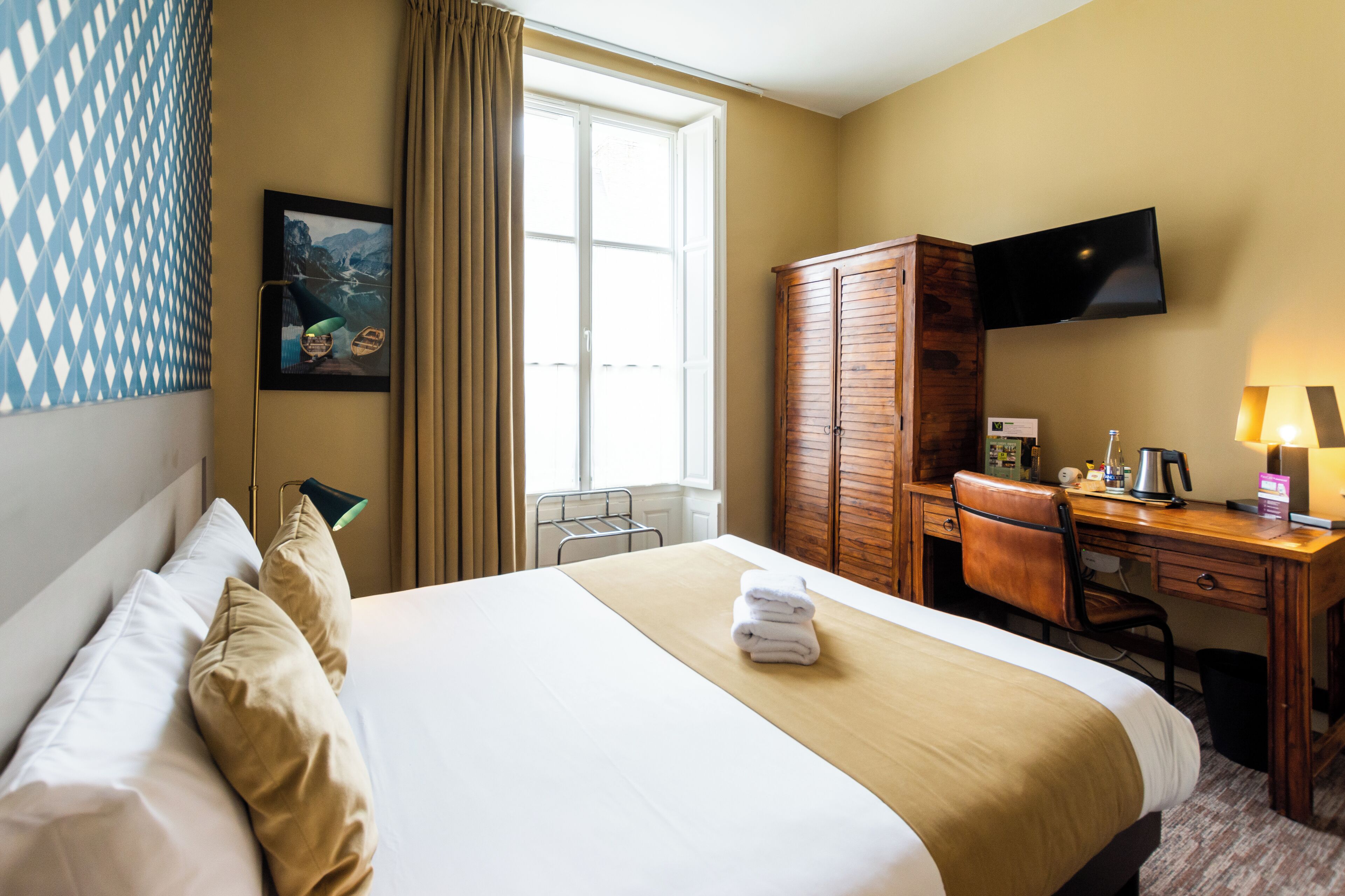 A hotel room with a large bed, a desk, a television, and a window with curtains.