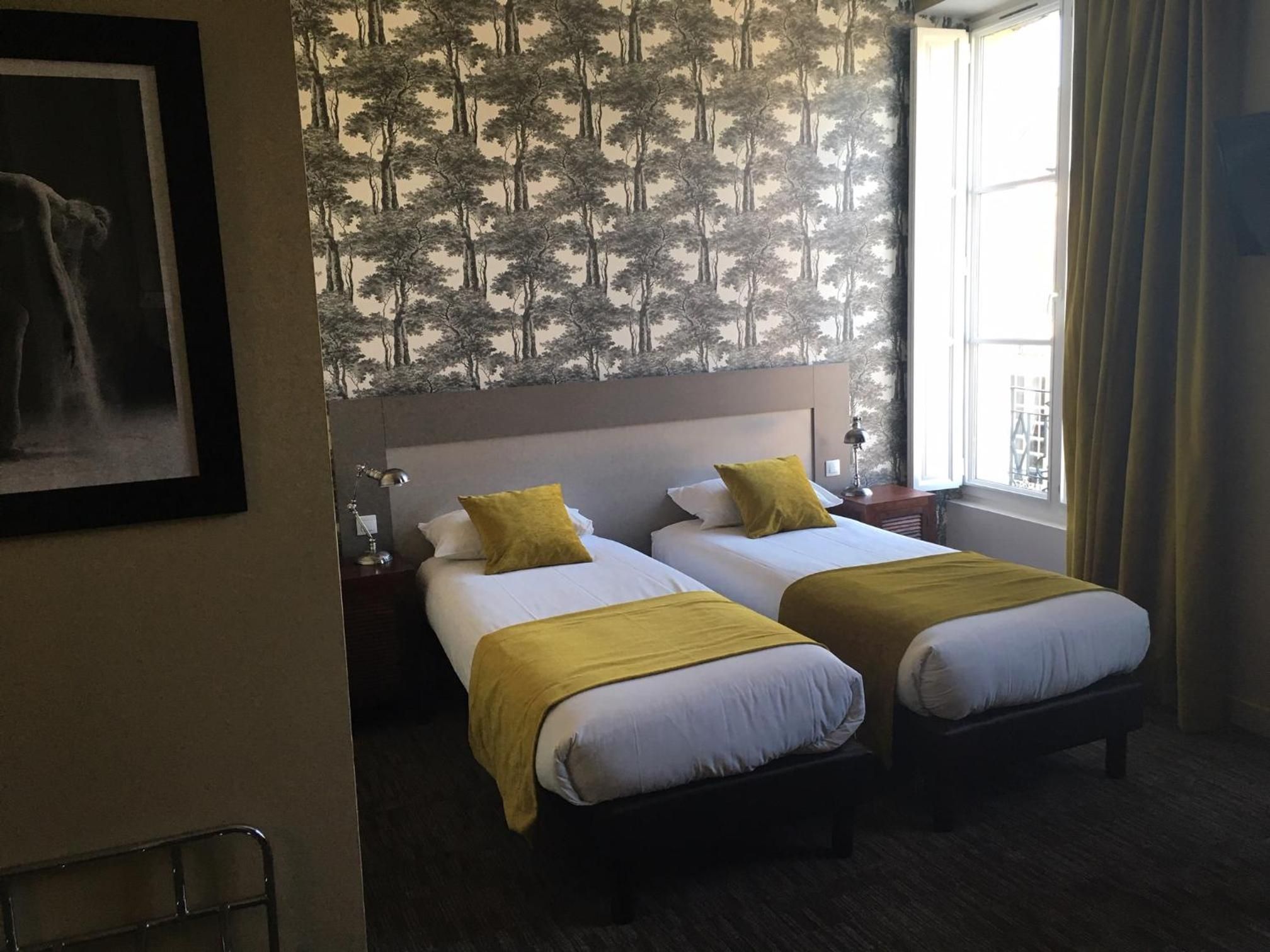 Habitación de hotel con dos camas, una mesita de noche, una lámpara y una ventana con cortinas.