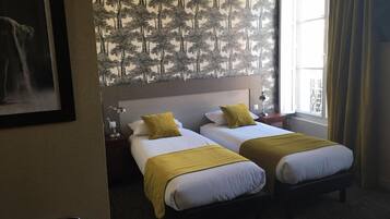 Habitación de hotel con dos camas, una mesita de noche, una lámpara y una ventana con cortinas.