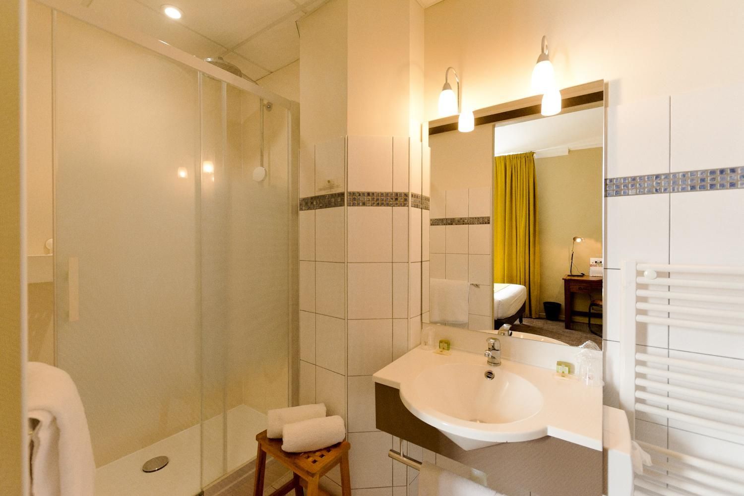 Een badkamer met een douche met glazen wand, een wastafel met spiegel en een handdoekrek.