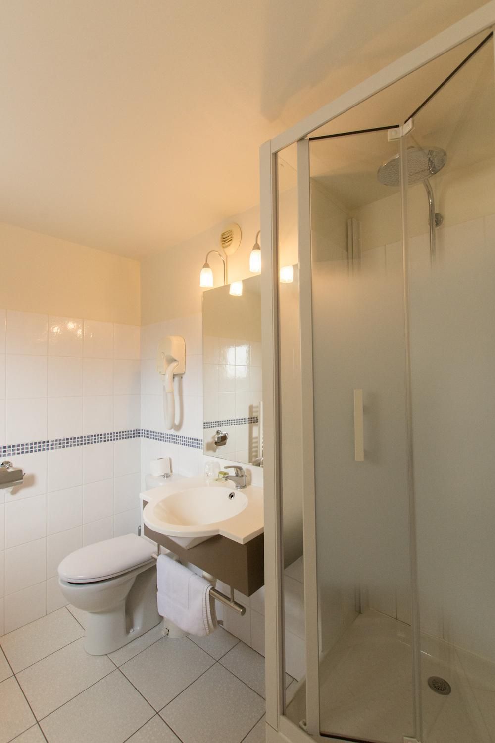 Un baño con inodoro, lavamanos y ducha con mampara de vidrio.