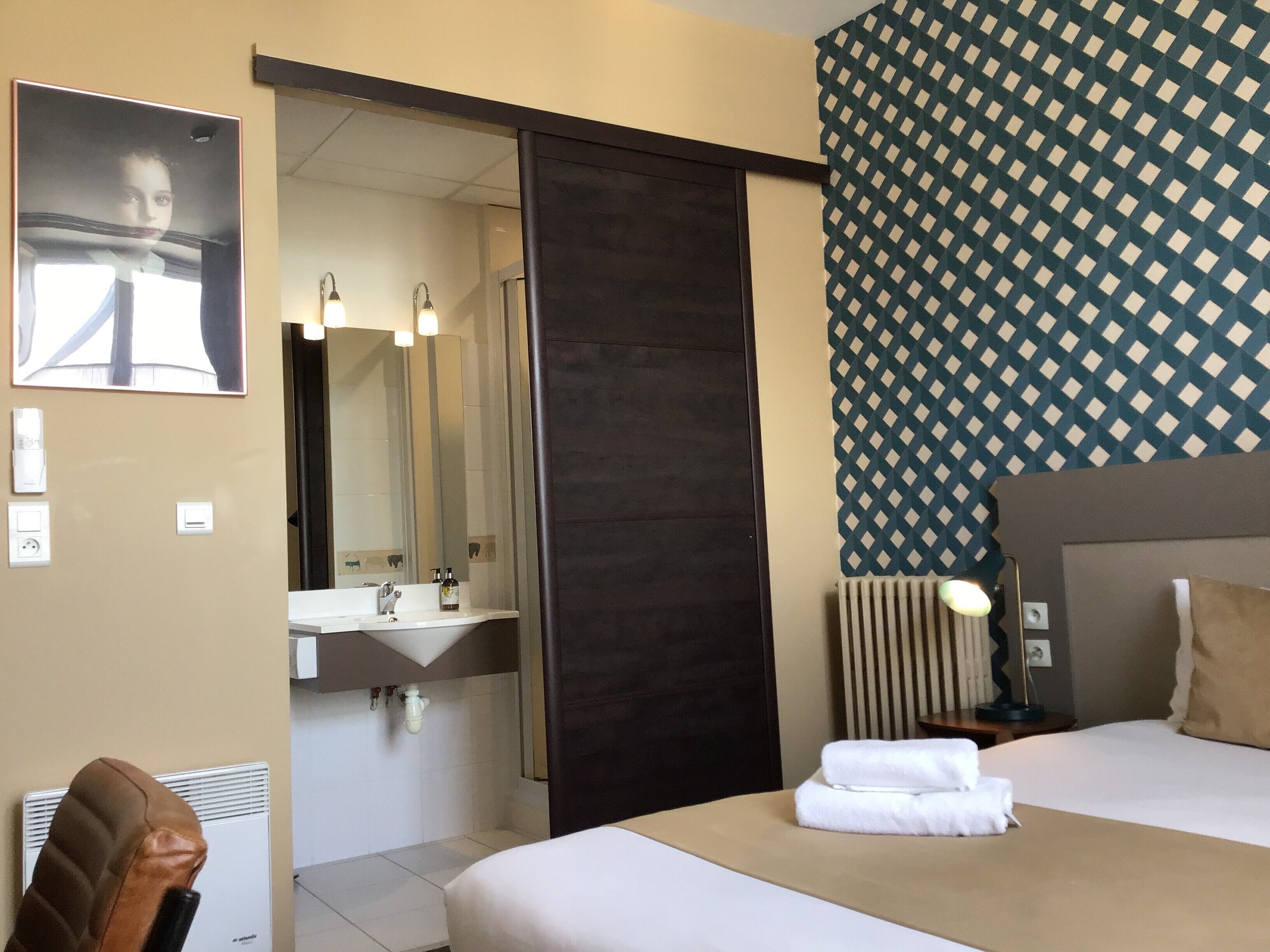 Habitación de hotel con cama, baño con lavamanos, espejo y pared con diseño.