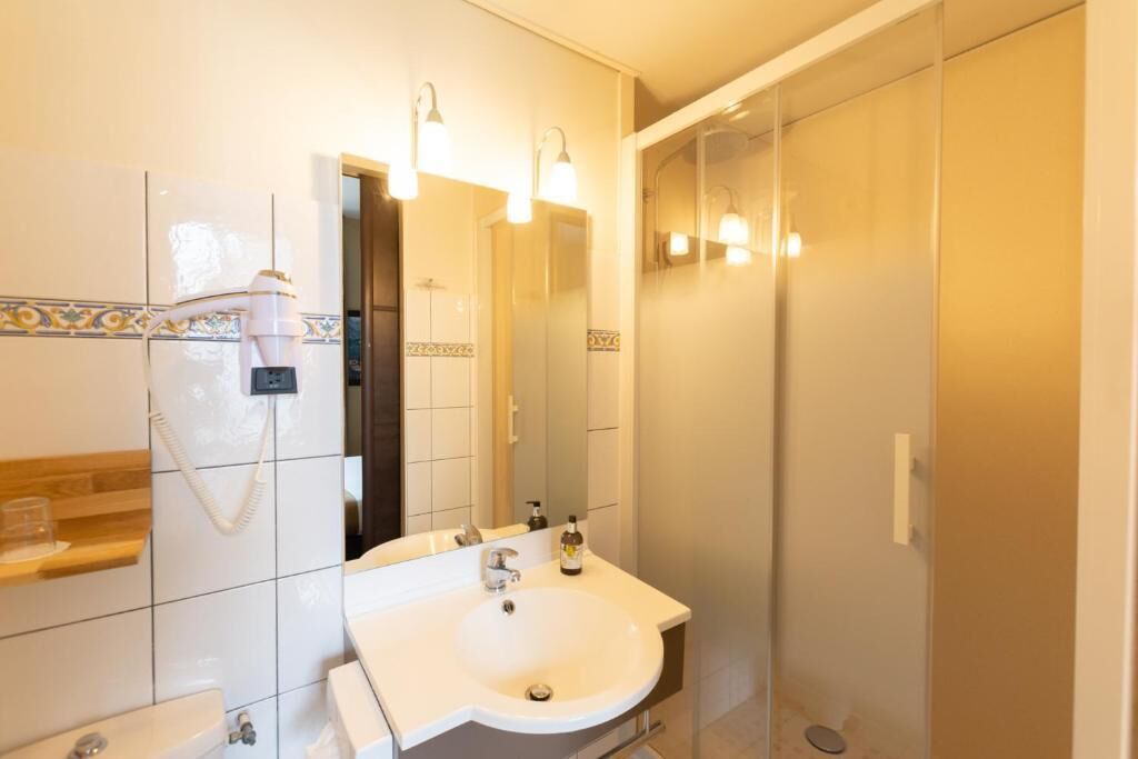 Un baño con lavamanos blanco, espejo, toallero y zona de ducha.