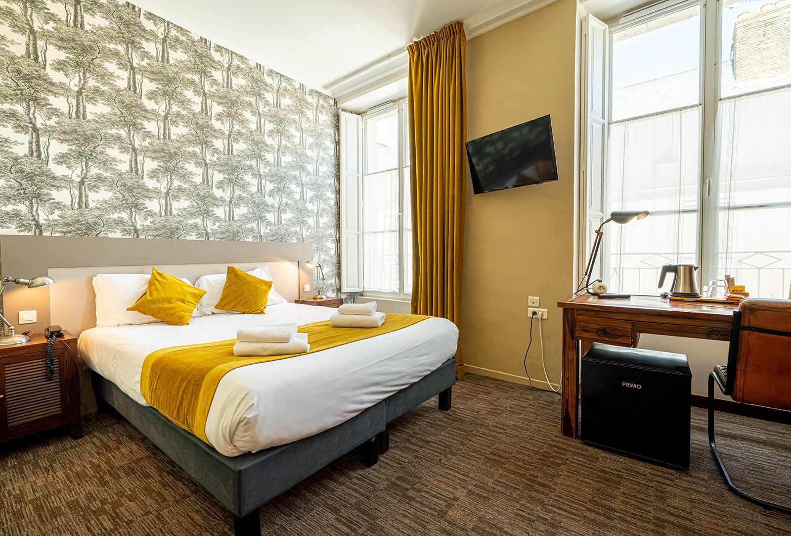 A hotel room with a bed, a desk, a television, and a window with curtains.