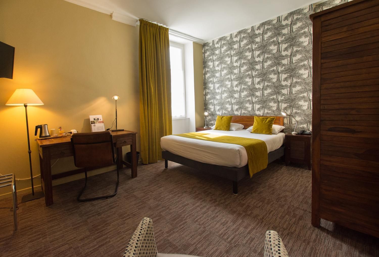 Ein Hotelzimmer mit Bett, Schreibtisch, Stuhl, Lampe und einem fensterbelagten Fenster.