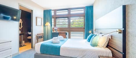 Habitación de hotel con cama, escritorio, silla, televisor y ventana con cortinas.
