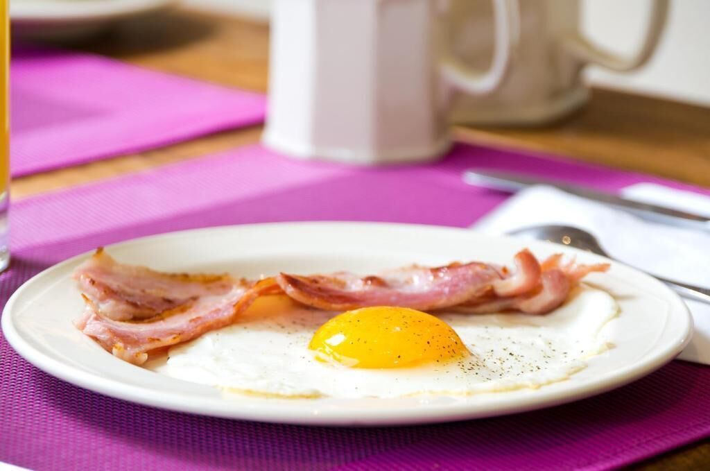 A plate with a fried egg and bacon on a table with a pink placemat.
