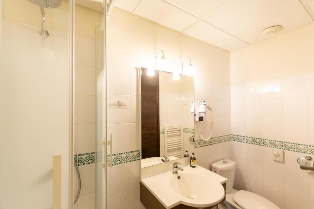 Un baño con ducha, lavabo, inodoro y un espejo con iluminación.