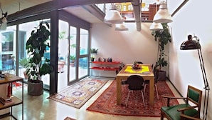 A spacious living area with a staircase, a dining table with chairs, a bookshelf, and a large window offering a view of the outdoors. - LoftVerona (Verona)