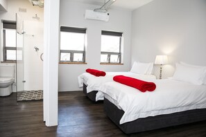 A hotel room with a large bed, two bedside tables, a window, a shower, and a toilet. - Zeederberg Corner (Paarl)