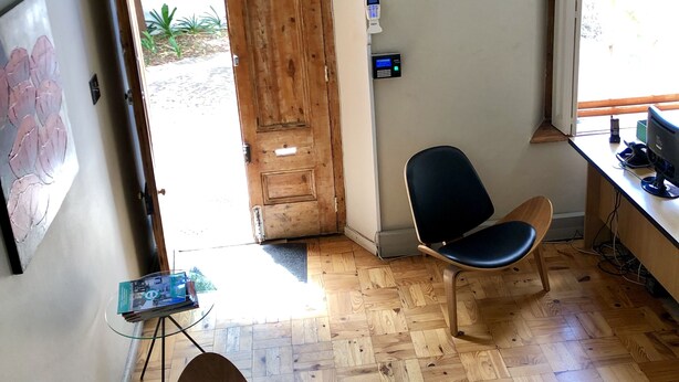 A room with a wooden door, two black chairs, a desk with a computer, and a window with blinds. - Zeederberg Corner (Paarl)