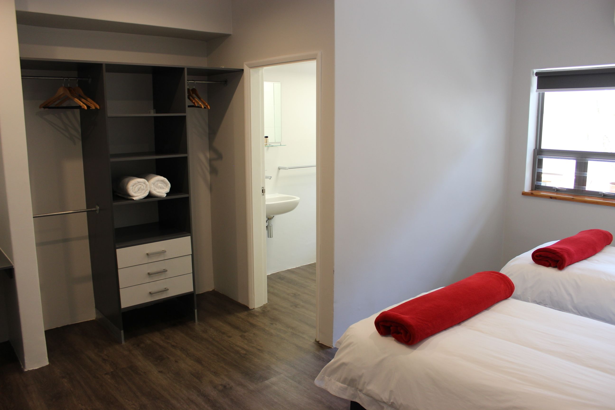 A hotel room with a wardrobe, a bed with red towels, and a view of the bathroom.
