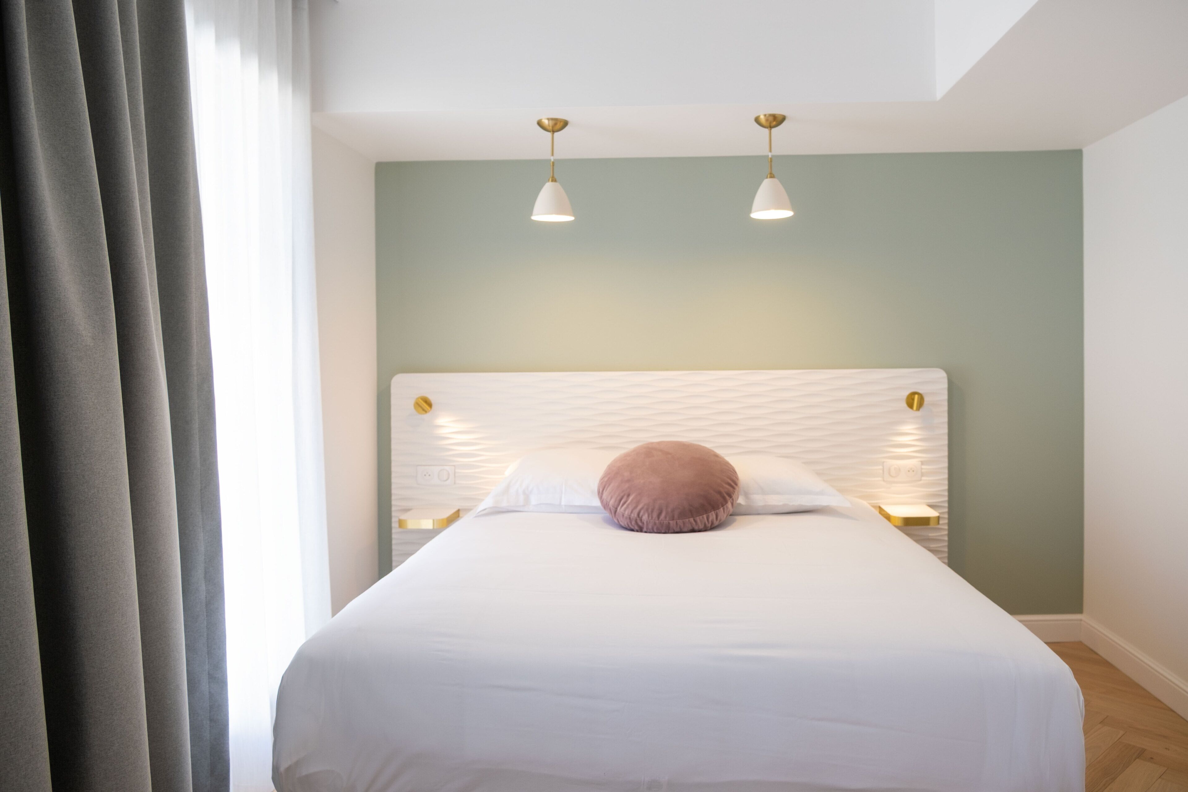 A neatly made bed with a white and pink pillow, two pendant lights, and a green wall.