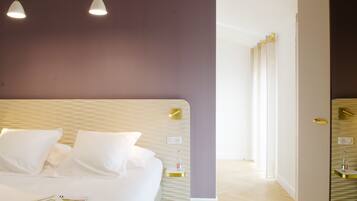 A modern bedroom with a large bed, white bedding, and a magazine on the bed. There are two pendant lights above the bed, and the room has a wooden floor and a purple accent wall.