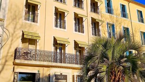 A hotel with multiple balconies, outdoor seating, and a palm tree. - Hotel Cafe Glacier Le XIX (Béziers)