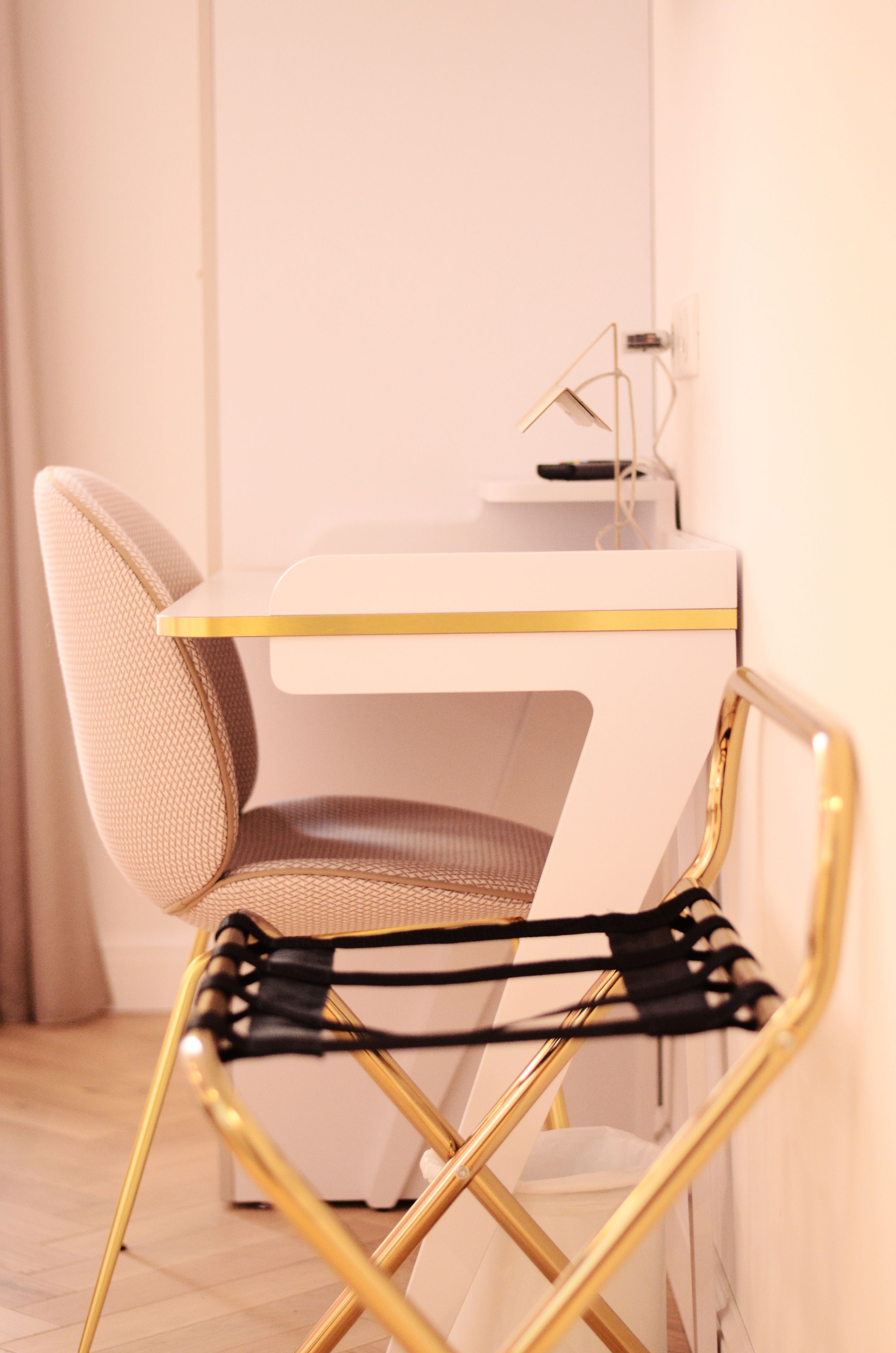 Une table blanche avec un bord doré et une chaise noire aux pieds dorés.