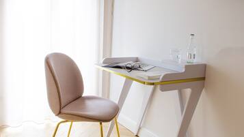 Een moderne kamer met een houten visgraatvloer, een wit bureau met gouden accenten, een bruine stoel en een groot raam met dunne gordijnen.