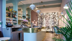 A modern bar area with a curved counter, shelves of bottles, and a patterned wall in the background. - Hotel Cafe Glacier Le XIX (Béziers)