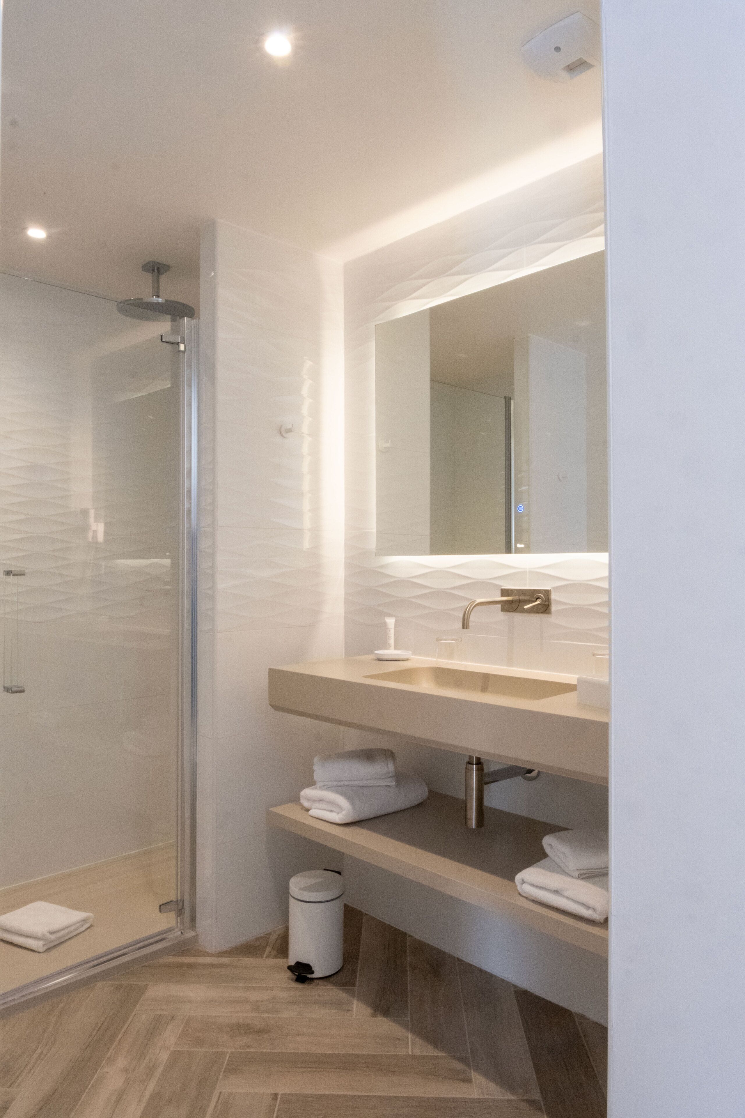 Un baño moderno con cabina de ducha de vidrio, un espejo grande y una encimera con lavabo y espacio para guardar toallas.