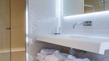 A modern bathroom with a glass shower enclosure, a white vanity with a mirror, and neatly folded towels on a shelf.