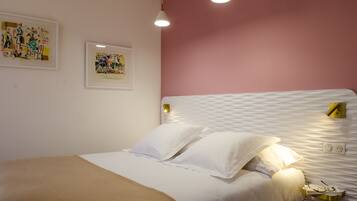 A neatly made bed with white linens and pillows, a bedside table with a lamp, and two framed artworks on the wall.