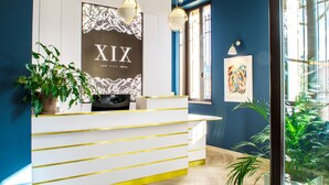 A hotel reception desk with a modern design, a large framed sign reading "XIX CAFE HOTEL", and potted plants. - Hotel Cafe Glacier Le XIX (Béziers)