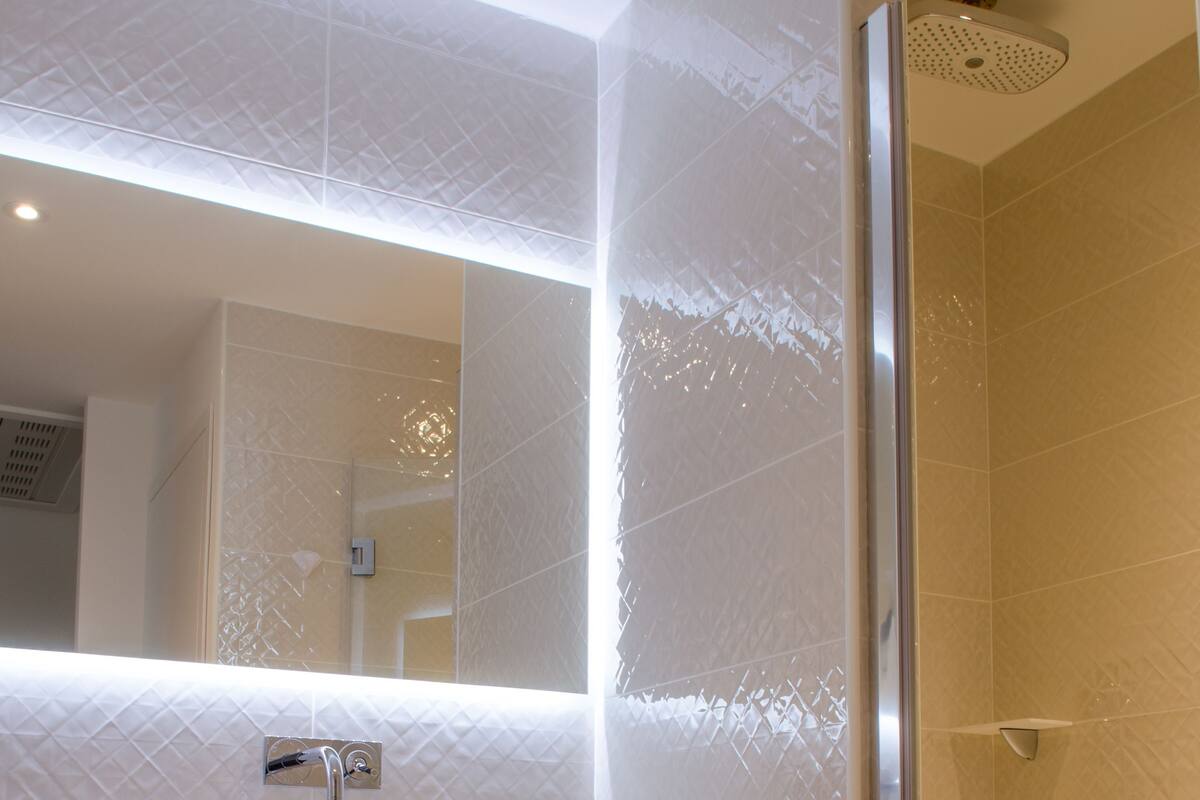 A bathroom with a glass shower enclosure, a white sink with a mirror above, and a shelf with folded towels.