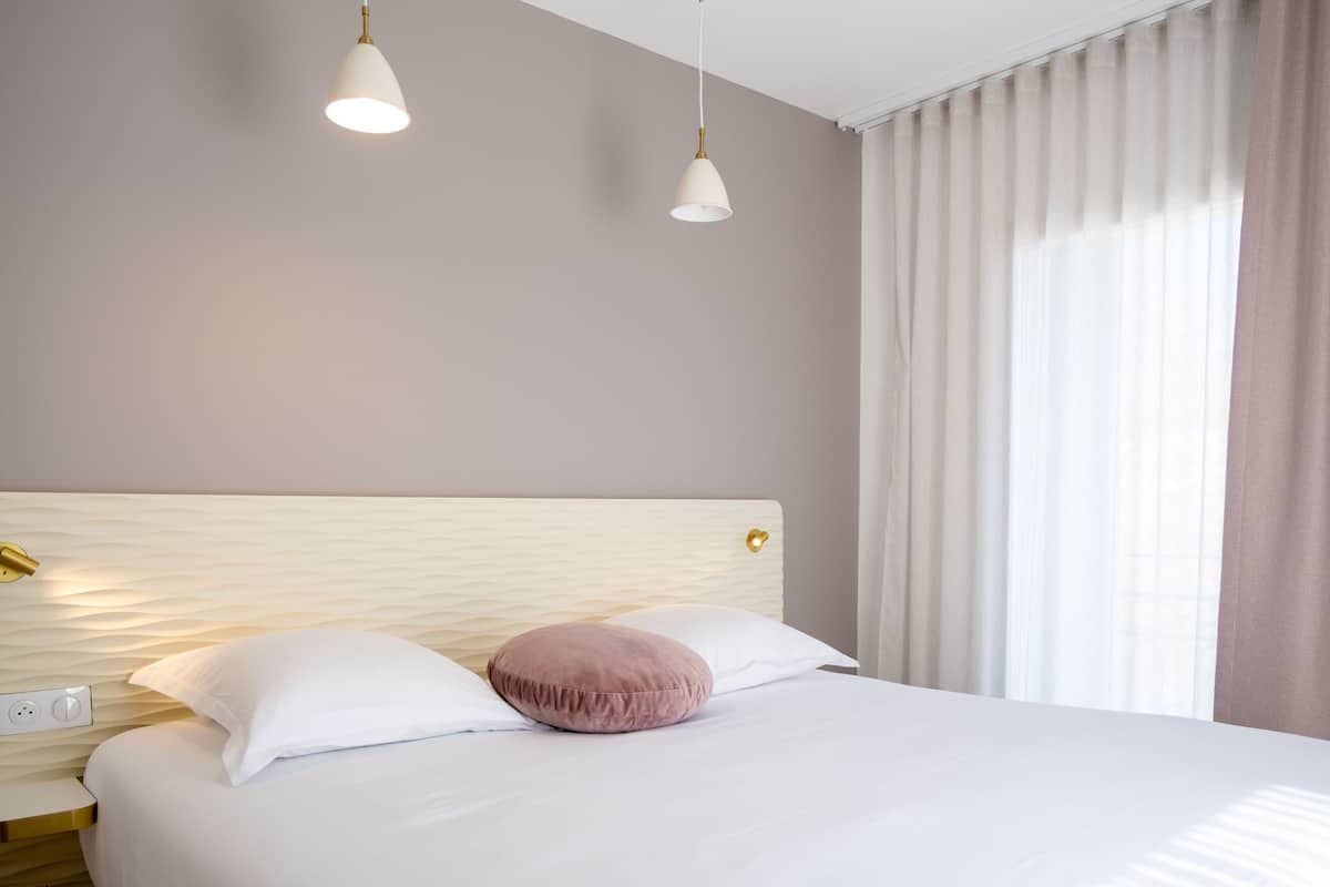 A neatly made bed with white and pink pillows, a textured headboard, and two pendant lights.