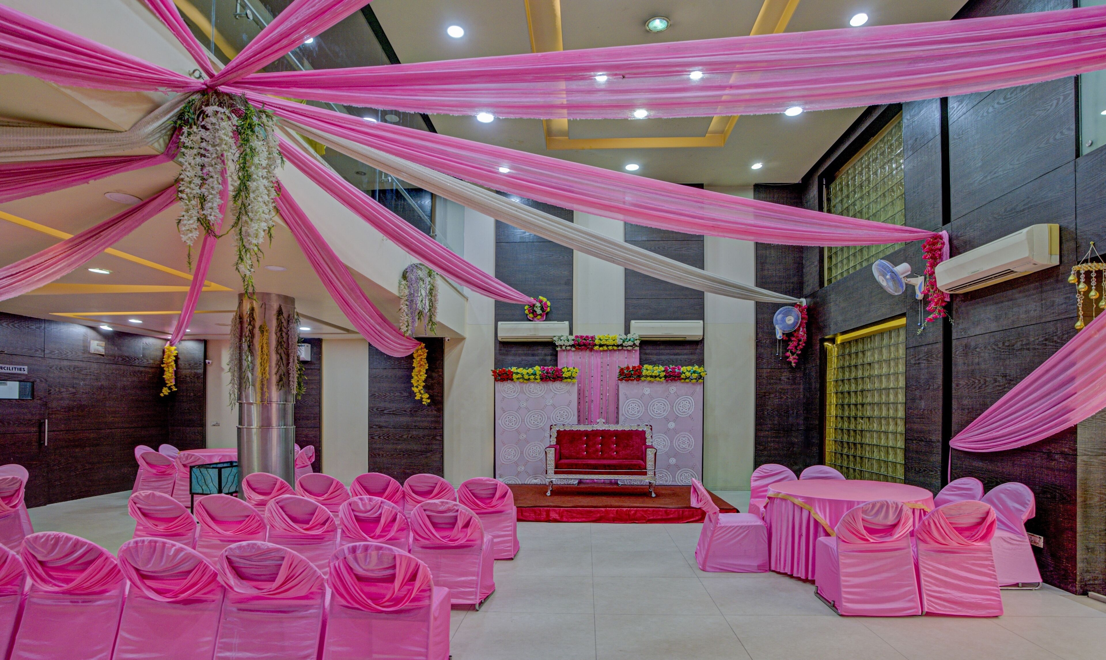 Um salão com tetos adornados em rosa, um palco central com fundo vermelho e fileiras de cadeiras revestidas de rosa.