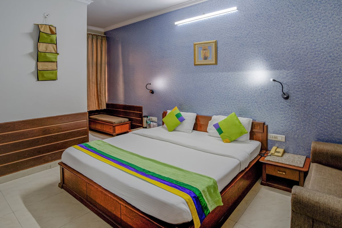 Habitación de hotel con cama de madera, mesita de noche, silla, teléfono en la pared y un marco de fotos.