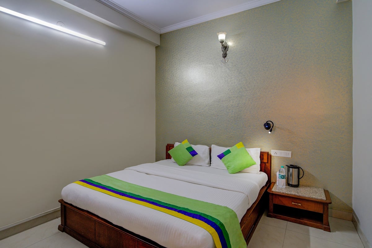 Una cama bien tendida con un edredón a rayas, una mesita de noche con lámpara y un aplique de pared.