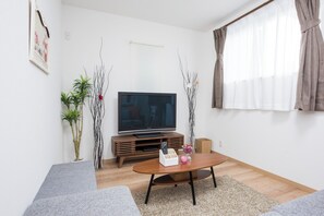 A modern living room with a flat-screen TV, wooden entertainment unit, grey sofa, and a coffee table with decorative items.