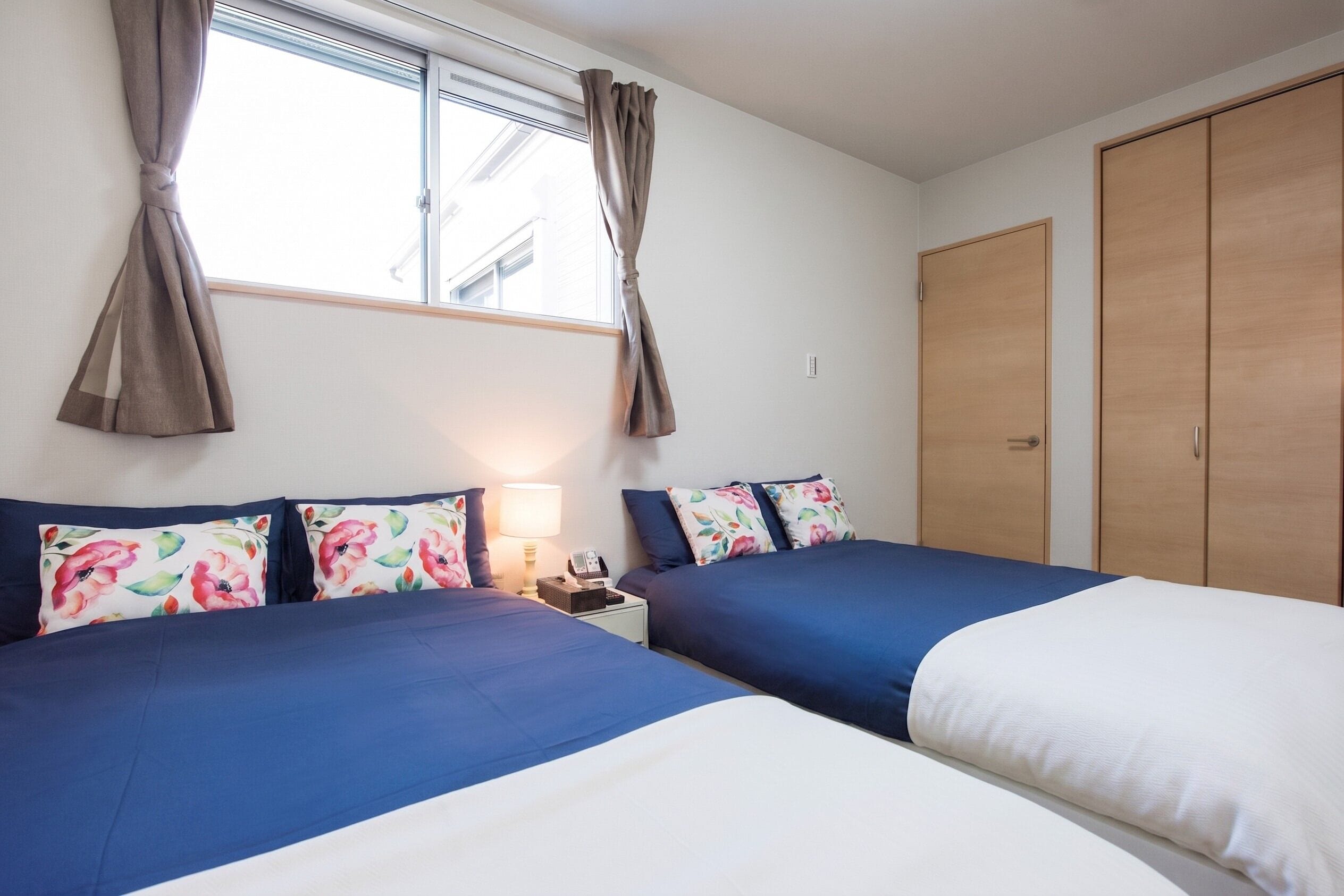 A hotel room with two beds, a nightstand, a lamp, a telephone, and a wardrobe.