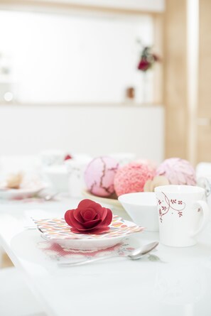 A table with a white tablecloth, a red rose, a white mug with floral designs, and pink macarons. - Tinker Bell (Osaka)
