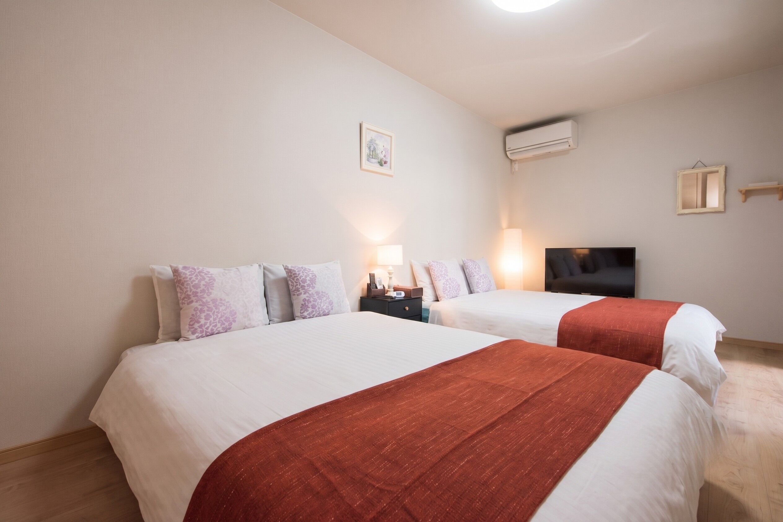 Et hotelværelse med to senge, et fjernsyn, et natbord med lampe og en aircondition.