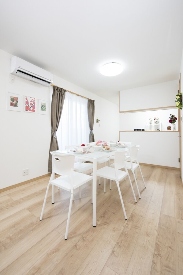 A dining area with a white table and chairs, an air conditioning unit on the wall, and a ceiling light. - Tinker Bell (Osaka)