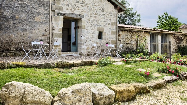 A stone building with a door and windows, a small garden with flowers and a lawn, and a stone wall. - La Grange d'Oustaud (Verac)