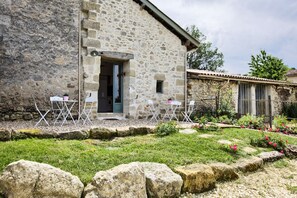 A stone building with a door and windows, a small garden with flowers and a lawn, and a stone wall. - La Grange d'Oustaud (Verac)