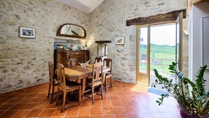 A rustic dining area with a stone wall, wooden furniture, and a view through a glass door. - La Grange d'Oustaud (Verac)
