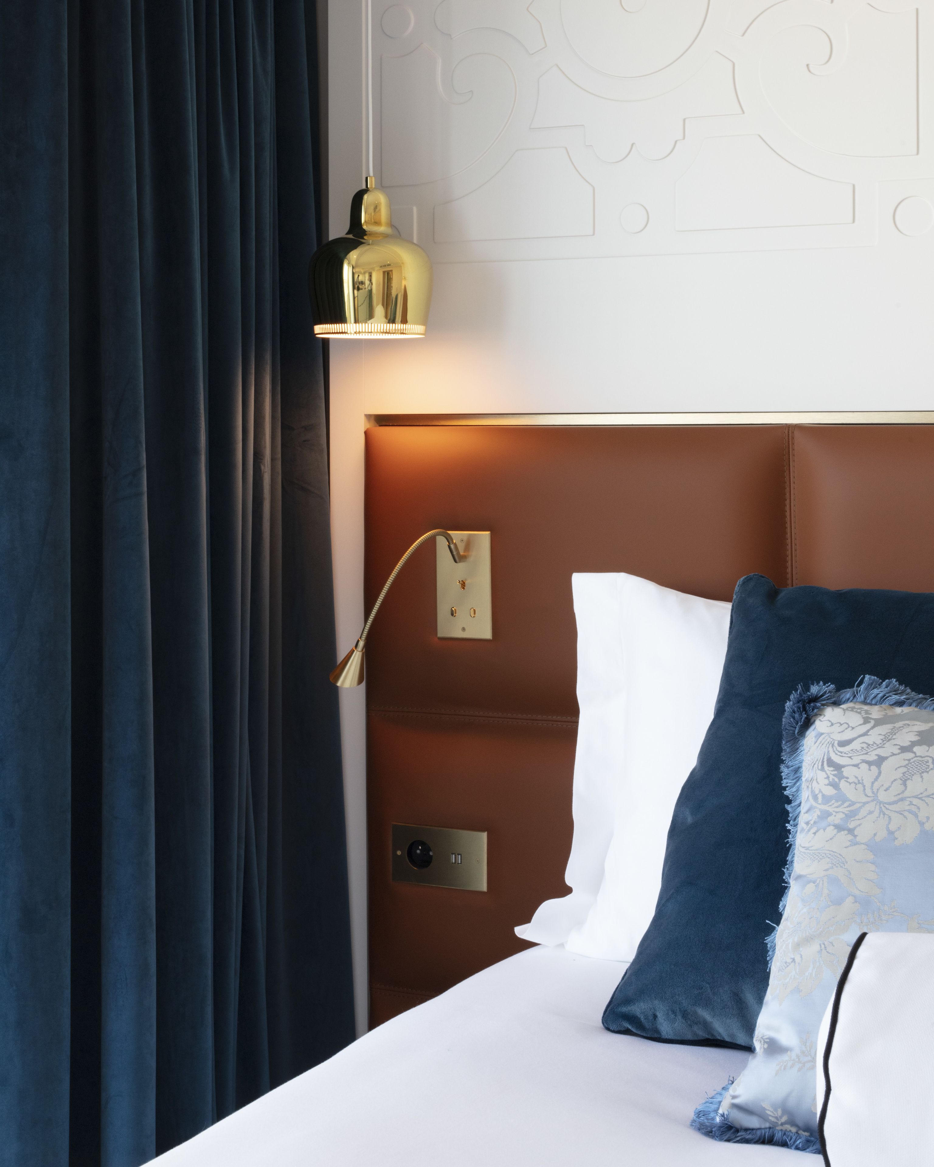 A hotel room with a bed, a nightstand, a wall-mounted lamp, and a power outlet.