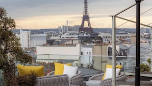A rooftop terrace with wicker furniture, a potted plant, and a view of the Eiffel Tower. - Hôtel Bowmann, a Small Luxury Hotel of the World (Paris)