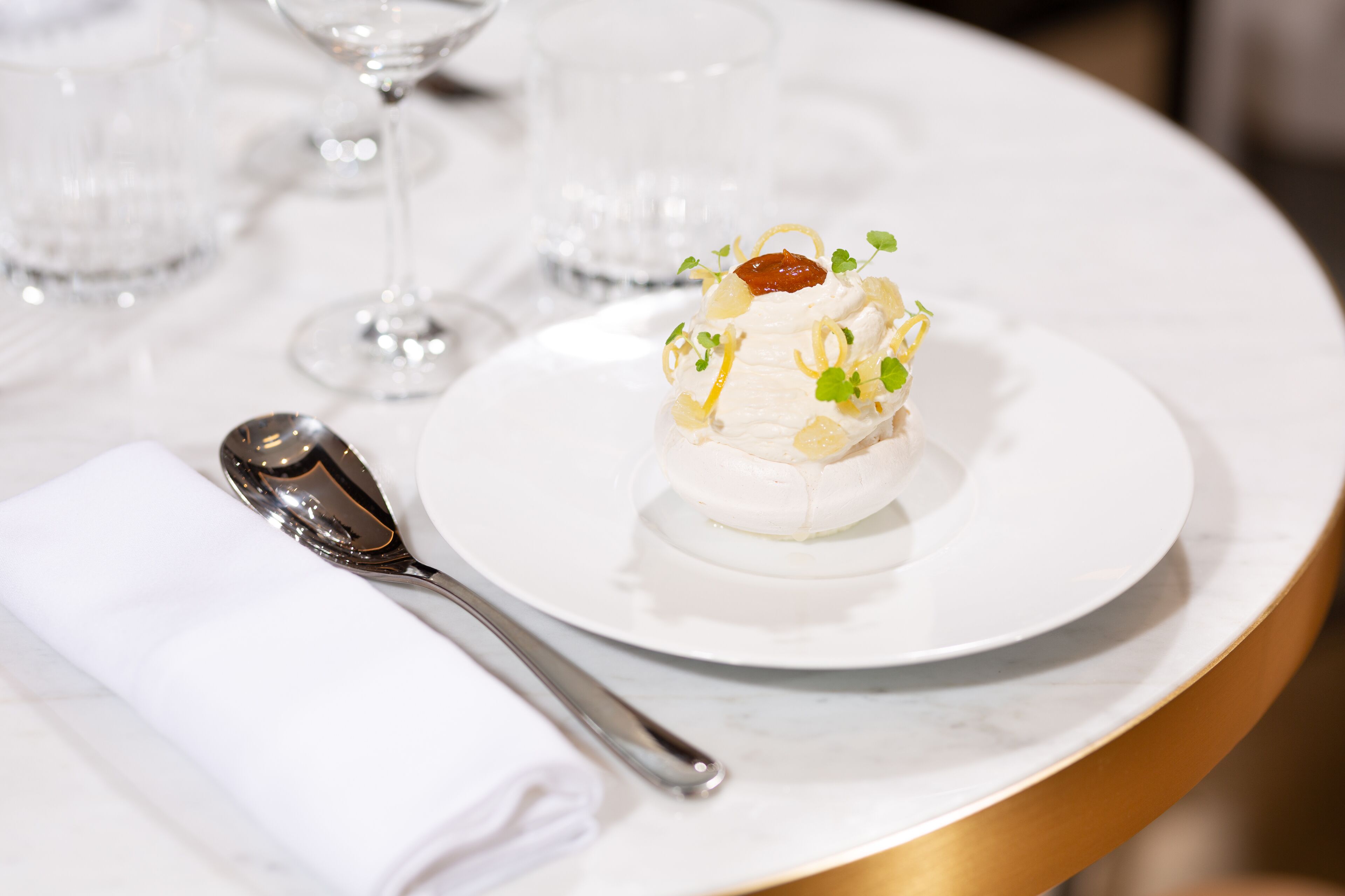 A white plate with a dessert on a marble table, accompanied by a folded napkin and a spoon.