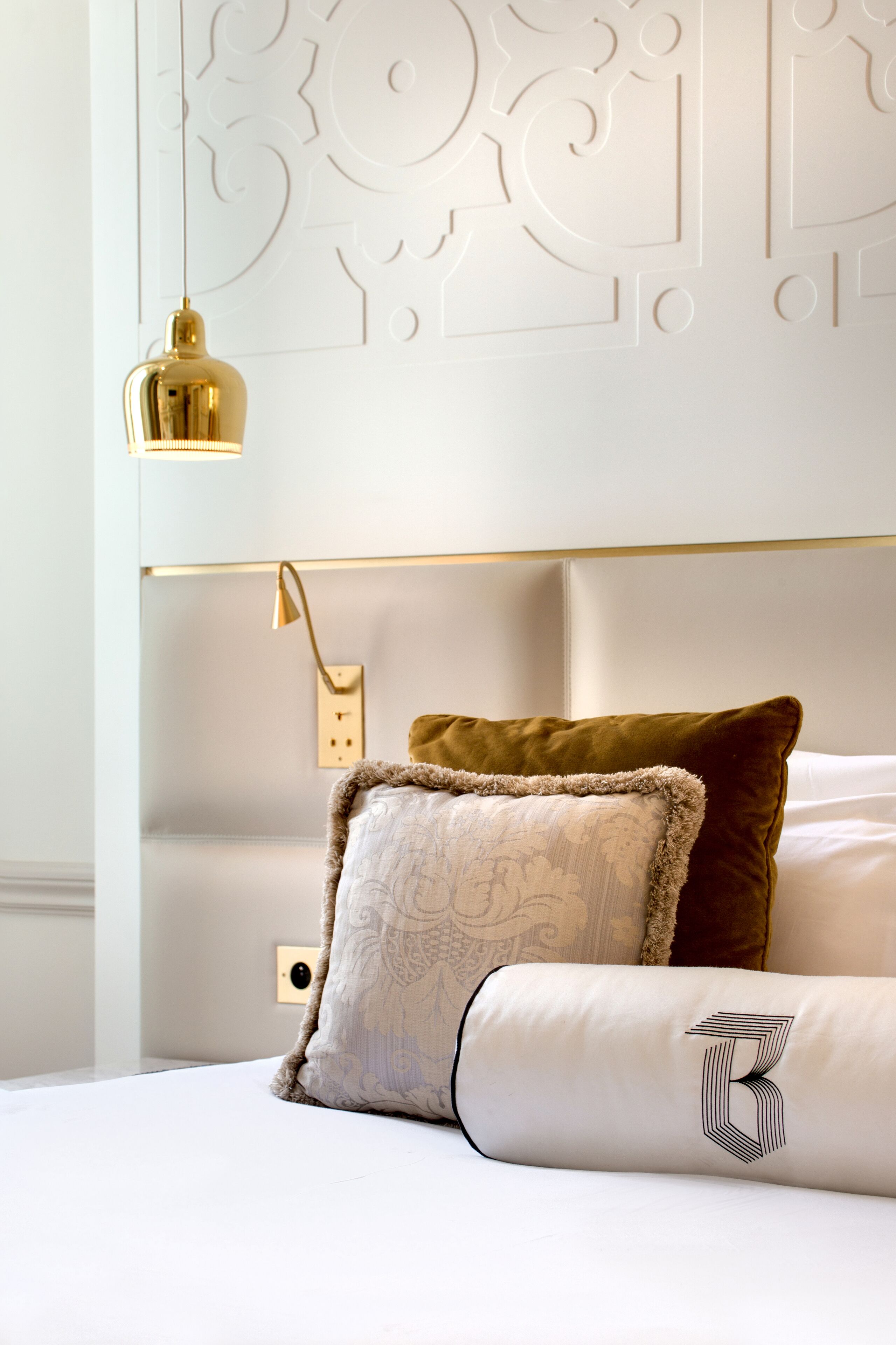 A neatly made bed with a decorative headboard, a gold lamp, and a patterned pillow.
