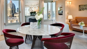 A modern hotel room with a round marble table, red upholstered chairs, a fireplace, and a view of a historic building. - Hôtel Bowmann, a Small Luxury Hotel of the World (Paris)