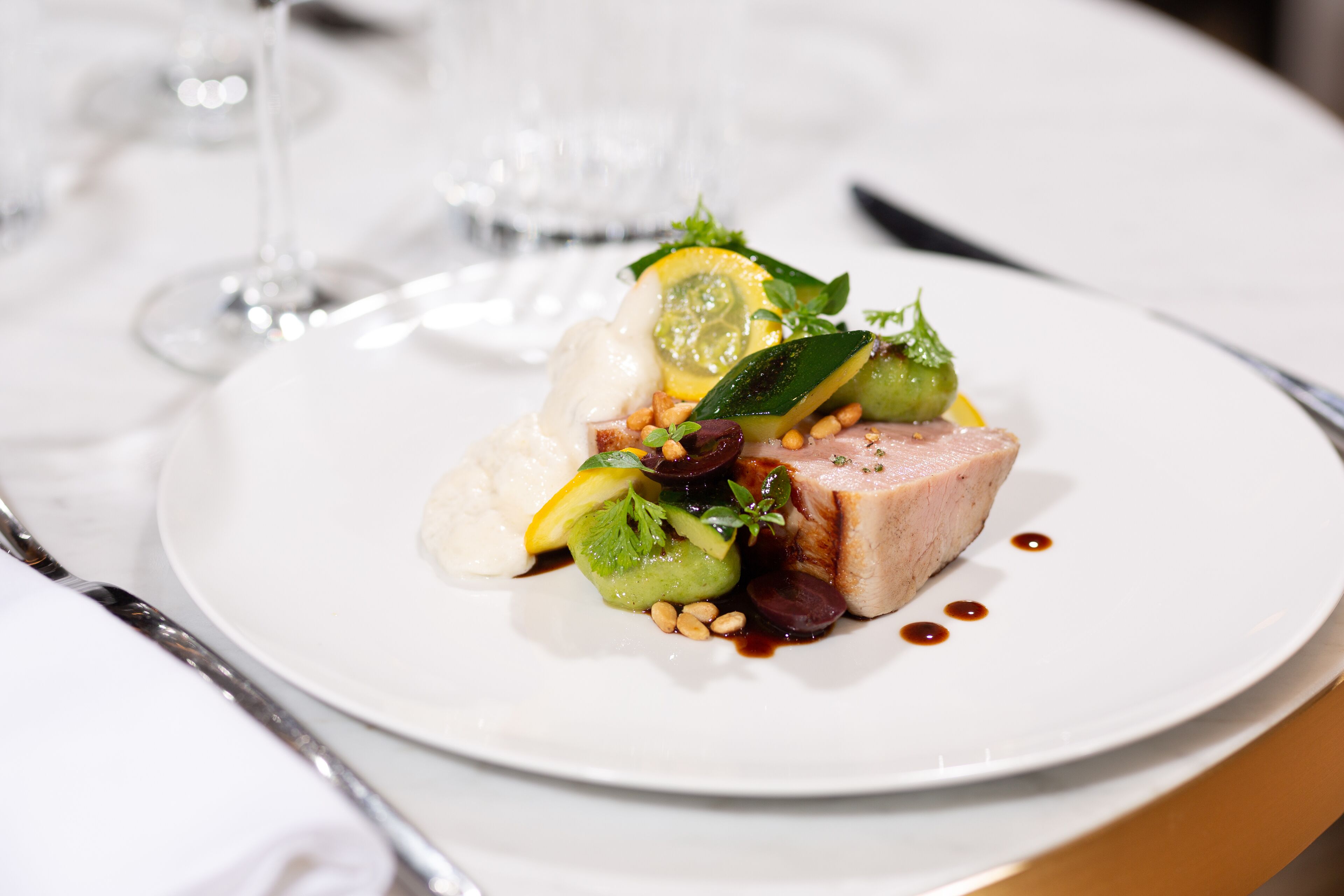 A white plate with a dish of food, including meat, vegetables, and a sauce.
