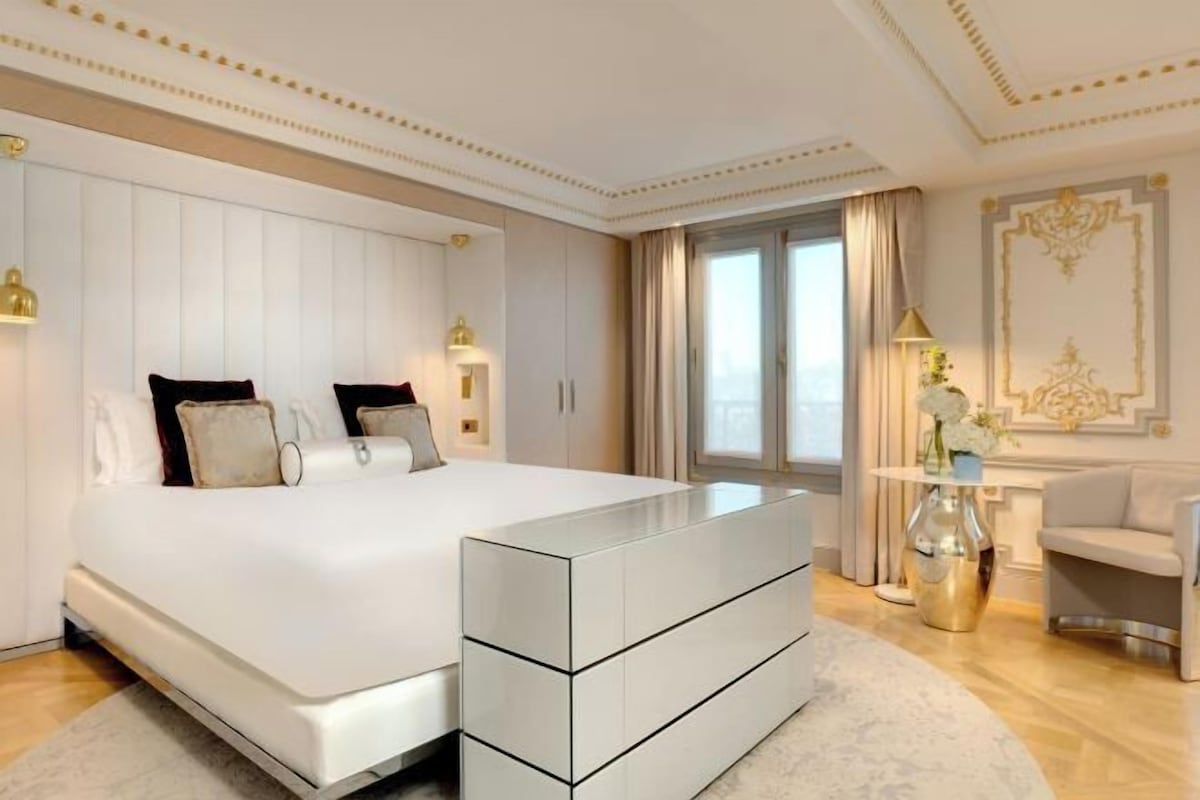 A modern bedroom with a large bed, a bedside table, a dresser, and a window with curtains.