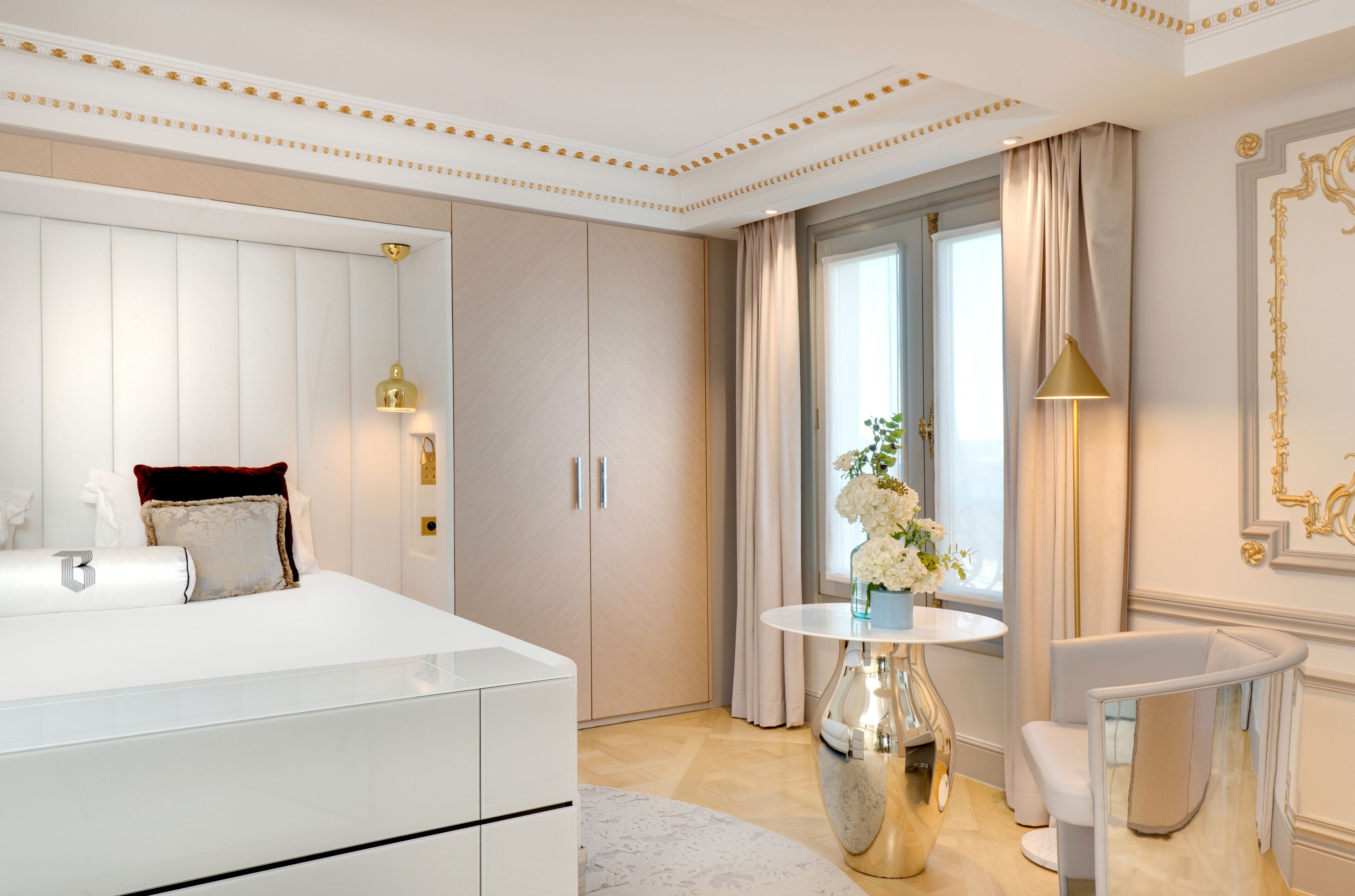 A modern bedroom with a large bed, a vanity, a round table with a vase, and a chair.